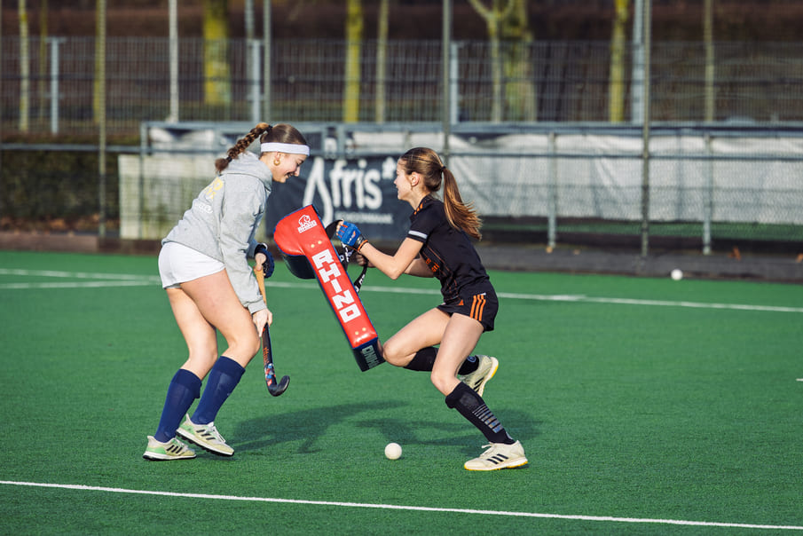 Twee vrouwelijke hockeyspelers trainen op het veld met ProHockey-hulpmiddelen tijdens een hockeykamp.