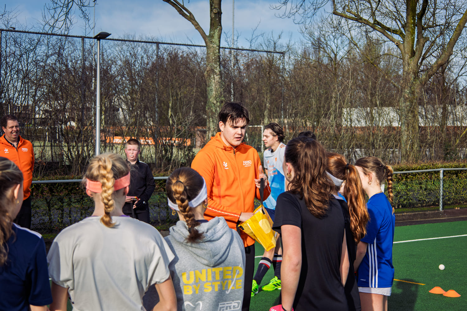 Jonge hockeyspelers luisteren naar een ProHockey coach tijdens een hockeystage op een buitenveld.