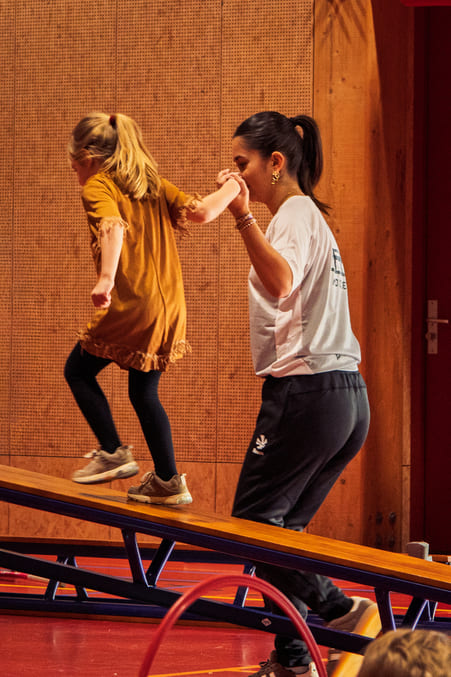 Kind en volwassene samen op houten plank tijdens ProHockey hockeikamp, begeleidende indoor activiteit.