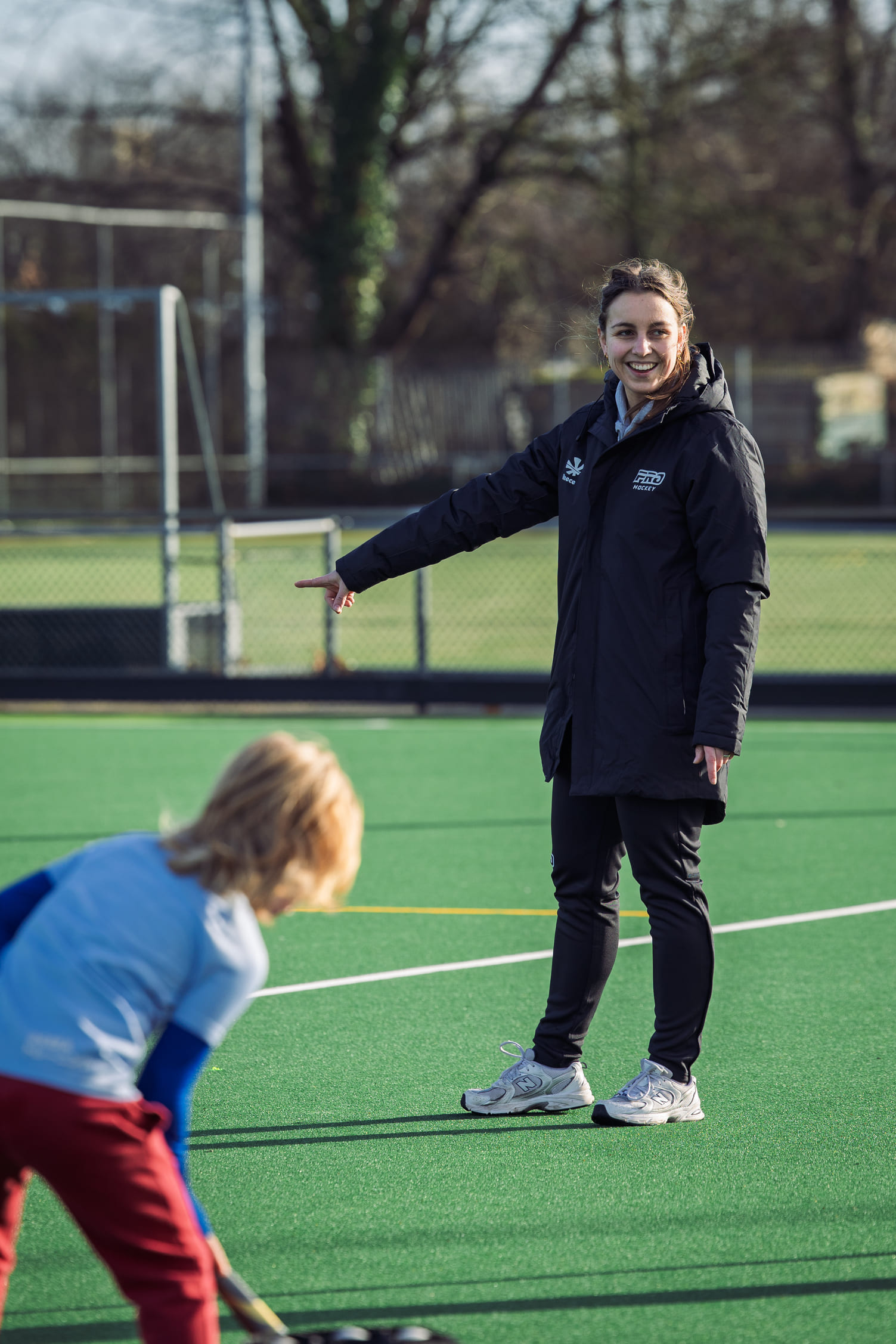 Vrouwelijke coach van ProHockey begeleidt jongere op hockeveld tijdens hockeykamp.