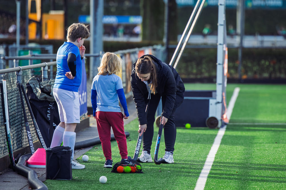 ProHockey hockekamp training met kinderen op hockeyveld, begeleid door coach. Kinderen leren hockeyvaardigheden.