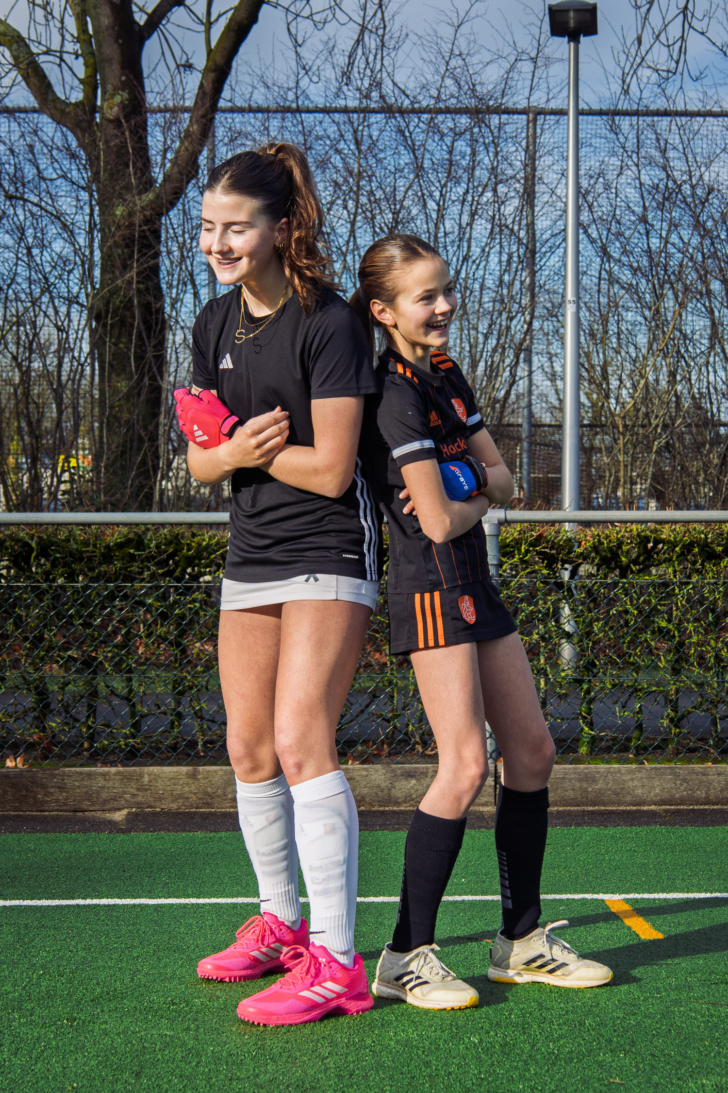 Twee lachende jonge vrouwen in hockeykleding poseren op een hockeyveld, als onderdeel van een ProHockey hockeikamp.