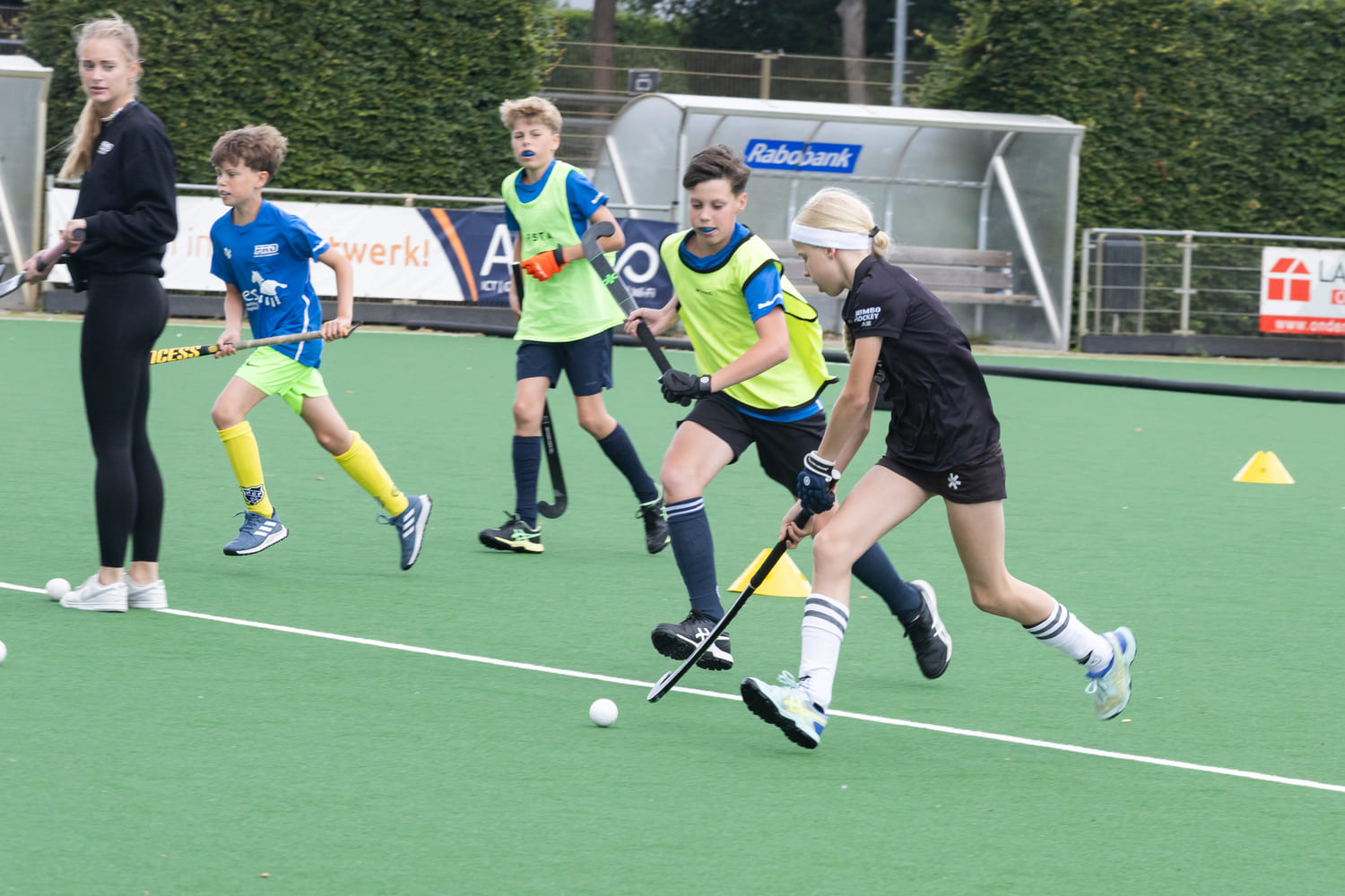 Jonge hockeyspelers in actie tijdens een ProHockey zomerkamp bij hockeyclub Prinsenbeek, gefocust op hun training op een groen kunstgrasveld.