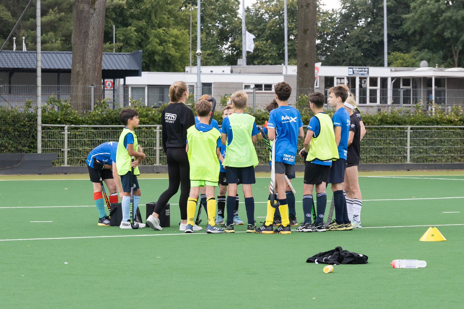 Kinderen ontvangen hockeytraining tijdens ProHockey zomerkamp bij hockeyclub Prinsenbeek, met sportuitrusting en begeleider op het veld.